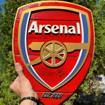Wooden Arsenal logo plaque held by a hand with a blurred natural background