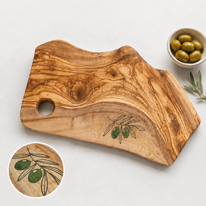Wooden cutting board with olive design and a bowl of olives on a light background